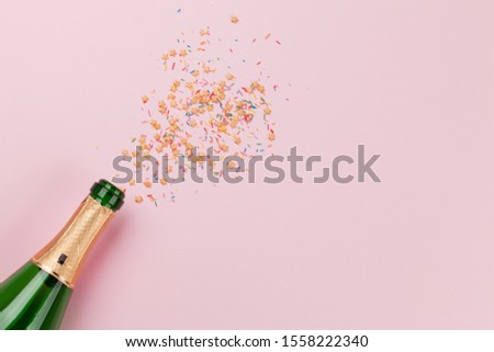 Christmas greeting card, champagne and star shaped sweets over pink background. Top view. Flat lay with space for your greetings