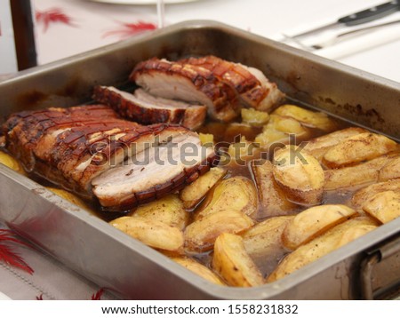 Homemade roast pork belly with fried potatoes sliced ​​in juice served in a roasting pan on a set table - Typical Austrian meal as a main course named Innviertler Bratl in der Rein Royalty-Free Stock Photo #1558231832