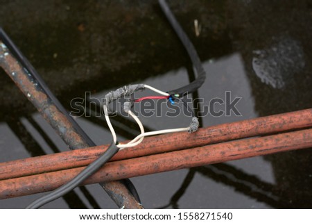 wires are interconnected and insulated with electrical tape on the street on the roof of the plant. beneath them is a puddle after rain. safety violation. danger of short circuit current Royalty-Free Stock Photo #1558271540