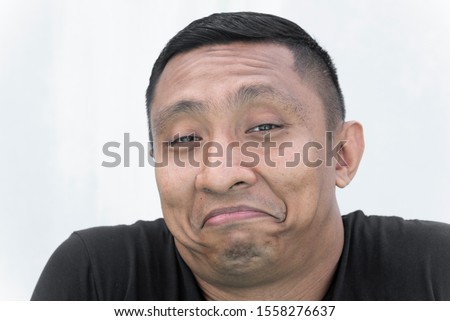 A portrait of the face of an Asian Indonesian male model who smiles and frown awkwardly at the same time AKA frown smile. Portrait on white background. Royalty-Free Stock Photo #1558276637