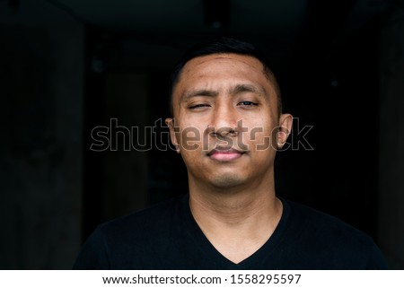 portrait on black of the face of an Indonesian Asian man on white background looking straight into the camera. He has short hair and it looks like a mug shot. His eyes  narrowed his lips sealed tight Royalty-Free Stock Photo #1558295597