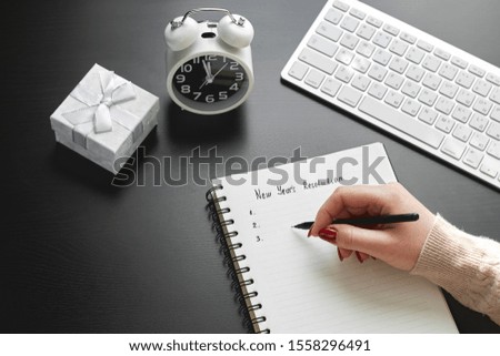 Woman's hand writes in an open notebook lying on black table with pen and notepad. Copy space on dark background. 