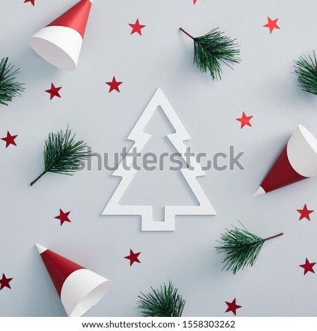 Christmas minimal concept - christmas composition with party cone, red star confetti and evergreen tree on pastel color background. White xmas tree silhouette. Design template on blue backdrop.