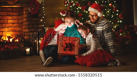 Merry Christmas! happy family mother father and children with magic gift near tree at evening at home
