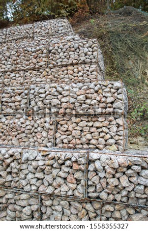 The mesh cells of the cubic form are filled with mountain stones of various shapes that let water through the rain, but protect the road from falling stones
