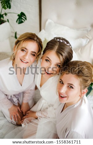 Bride with bridesmaids in bathrobes sitting on bed