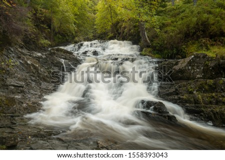 This is a picture from the Scottish Highlands on a cloudy day showing a waterfall in a beautful forest. 