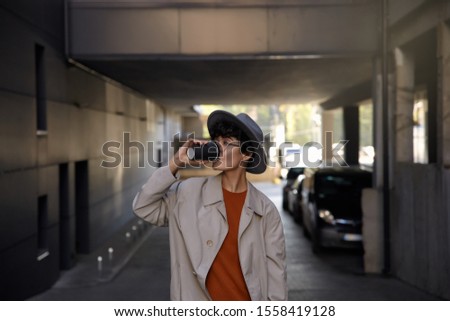 Outdoor shot of stylish young curly lady with short haircut drinking coffee while standing over city environment, wearing trendy clothes and wide grey hat