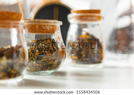 Glass jars with dry tea leaves close up on white table