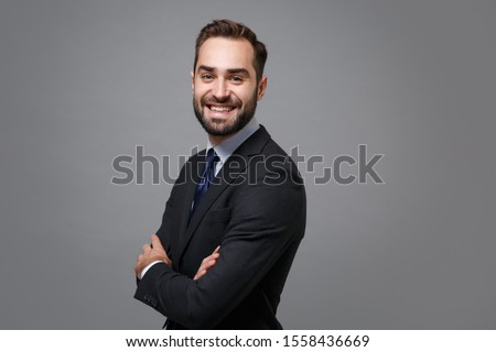 Side view of young business man in classic black suit shirt tie posing isolated on grey background. Achievement career wealth business concept. Mock up copy space. Hold hands crossed, looking camera.