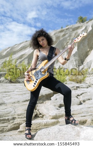 Woman play yellow bass guitar on sandy background