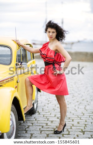 Woman in dress rely leg on yellow car