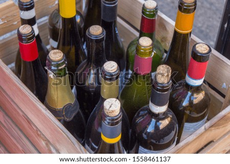 old glass wine bottles with corks and multi-colored labels in a wooden box close-up
