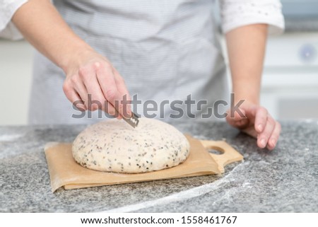 Baker making patterns on raw bread using a knife ot blade to shape the dough prior to baking. Manufacturing process of a bread at home
