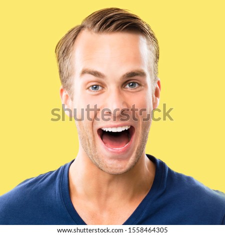 Portrait of happy excited man in blue clothing, isolated against yellow color background. Square composition.