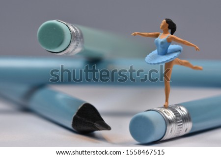 Miniature  ballet dancer with blue dress is dancing making a pirouette on a blue pencil (concept)