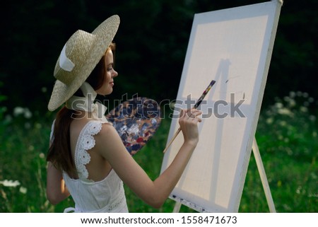 young woman in a clearing with a white canvas paints a picture