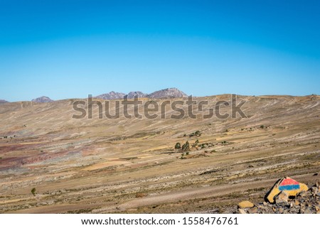 The dry grass fields inside Maragua Crater spread right to the rocky edge on a clear blue sky day.