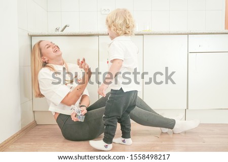 a cheerful mother and a joyful child sit on the floor in white t-shirts and paint each other with paints