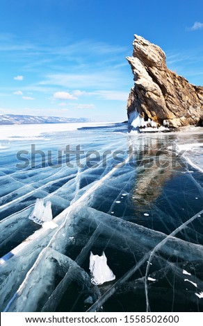 Baikal Lake. Small Sea Strait at cold sunny day. Beautiful blue slippery ice with cracks near famous Dragon Rock on edge of Ogoy Island - a natural landmark. Ice travel on frozen lake (focus on ice)