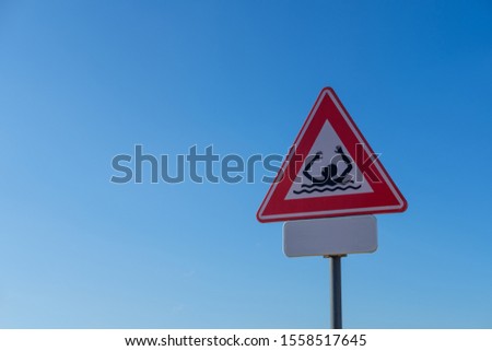 Danger of drowing sign with a blue sky in the background. Forbidden to swim symbol. Caution sign triangle with red border and drown icon.