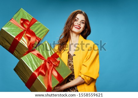 Beautiful woman with gift boxes in hands on a blue background and a yellow holidays jacket