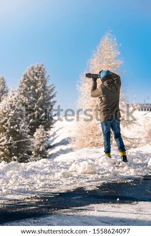 Men photographer taking pictures of winter scene, captured from behind in the Italian Alps during winter season .