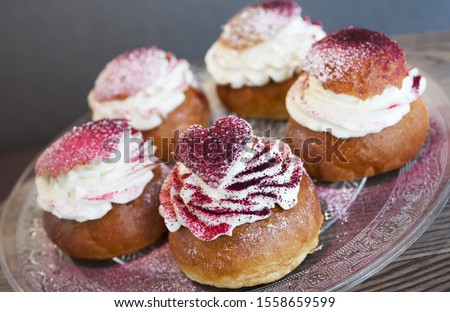 Closeup photo of five semlas on glass plate, gray background. Traditional  buns with whipped cream made for Shrove Tuesday, here finished with berry powder, instead of powdered sugar. Royalty-Free Stock Photo #1558659599