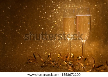 Two glasses of champagne decorated streamers on golden glittering background. Christmas and New Year holidays concept. Copy space.