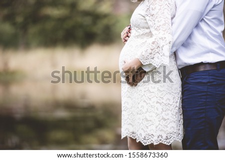 A closeup shot of a pregnant couple with their hands on the belly and a blurred background