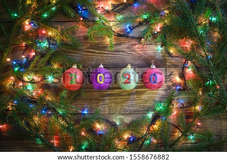 Cozy winter picture with Christmas tree branches, colorful lights and balls with 2020 on a wooden background