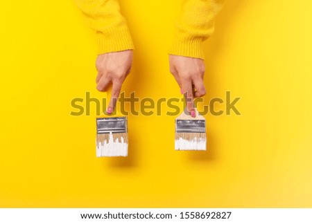 Paint brush in the hand of a girl on a yellow background, concept of apartment repair and painting works