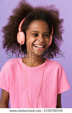Image of a positive optimistic happy young african girl kid posing isolated over purple wall background listening music with headphones.