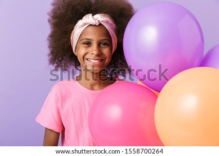 Image of a cute happy young african girl kid posing with balloons isolated over purple wall background.