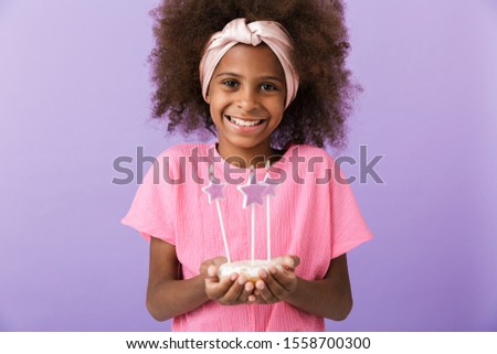 Image of a happy optimistic positive young african girl kid posing isolated over purple wall background holding birthday cake with candles.