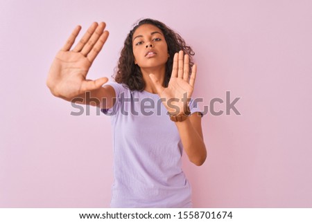 Young brazilian woman wearing t-shirt standing over isolated pink background doing frame using hands palms and fingers, camera perspective
