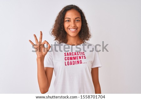 Brazilian woman wearing fanny t-shirt with irony comments over isolated white background doing ok sign with fingers, excellent symbol