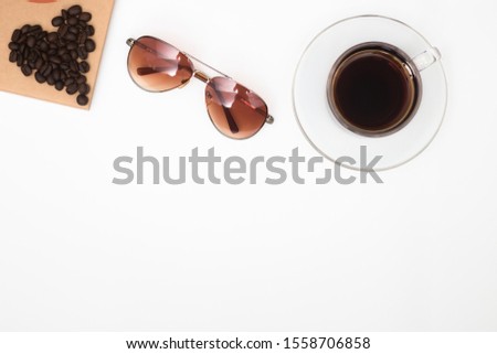 A cup of coffee on a white background and with coffee beans placed in a heart shape.