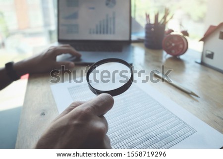 Business man using magnifying to review balance sheet annual with using  laptop computer to calculating budget. audit and Check integrity before investment concept.