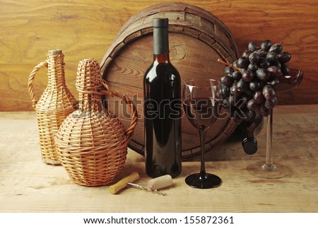 One glass of red wine, three bottles, grapes and oak barrel.  Wooden background 