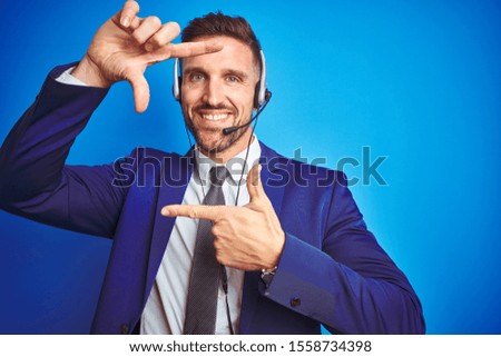 Young handsome operator man wearing call center headset over blue isolated background smiling making frame with hands and fingers with happy face. Creativity and photography concept.