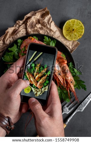 A man holds a smartphone in his hands and makes a photo of food. Tiger prawns on a gray background.