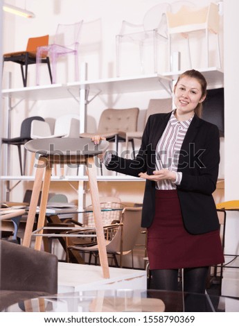 Young attractive saleswoman offering various of bar stools in furniture store