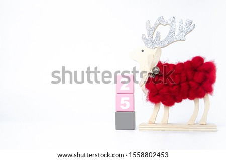 Red-haired deer-shaped wooden doll.Gray and pink wood blocks on the floor.Yellow gift boxes, yellow balls and green Christmas trees resting on a white background.Christmas concept.