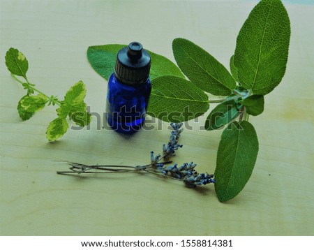 blue bottle pictured alongside herbs sage, lemon balm and lavender on wooden background 