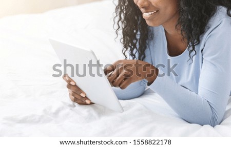 Cropped image of black girl holding digital tablet, laying on bed, relaxing on day off, entertainment application, free space