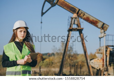 Woman engineer working near an oil pump. Young female engineer doing research near an oil pump unit noting information data in digital tablet. Industry Petroleum Engineer Woman Work on Digital Tablet