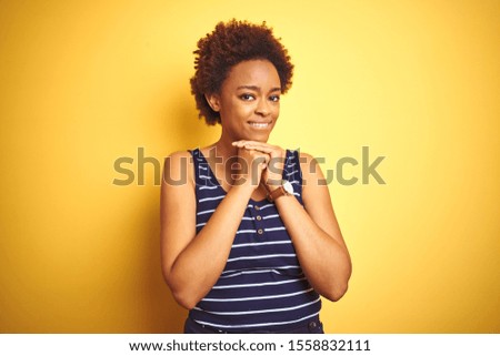 Beauitul african american woman wearing summer t-shirt over isolated yellow background laughing nervous and excited with hands on chin looking to the side