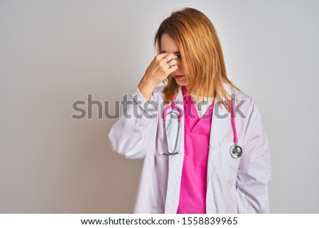 Redhead caucasian doctor woman wearing pink stethoscope over isolated background tired rubbing nose and eyes feeling fatigue and headache. Stress and frustration concept.