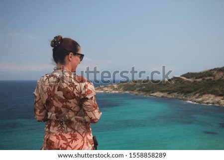 Summer lifestyle portrait of pretty woman. Standing on the cliff and looking to the sea. The sea is in the background.